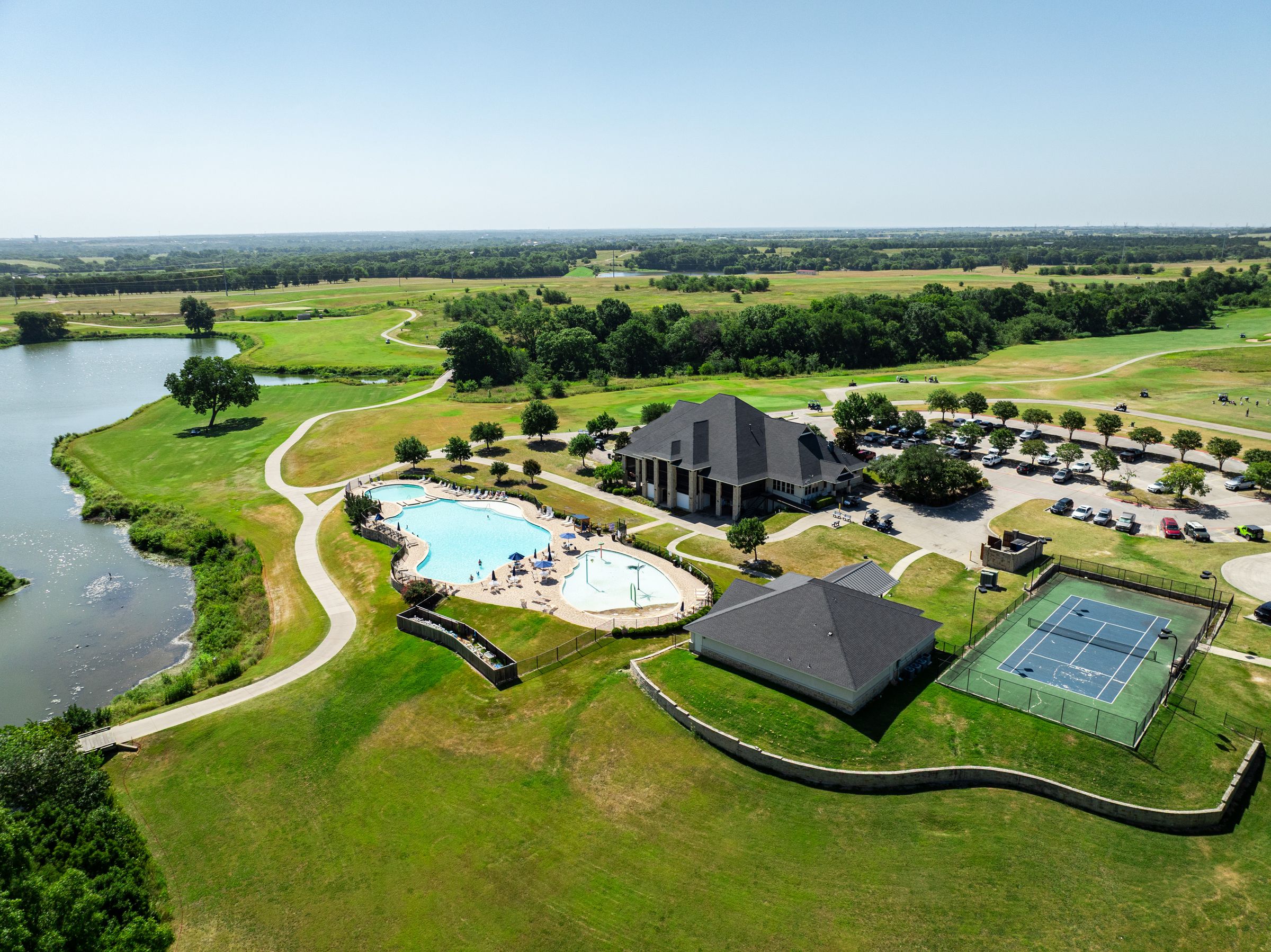 Clubhouse, resort-style pool and tennis courts beside a lake at The Bridges at Preston Crossings