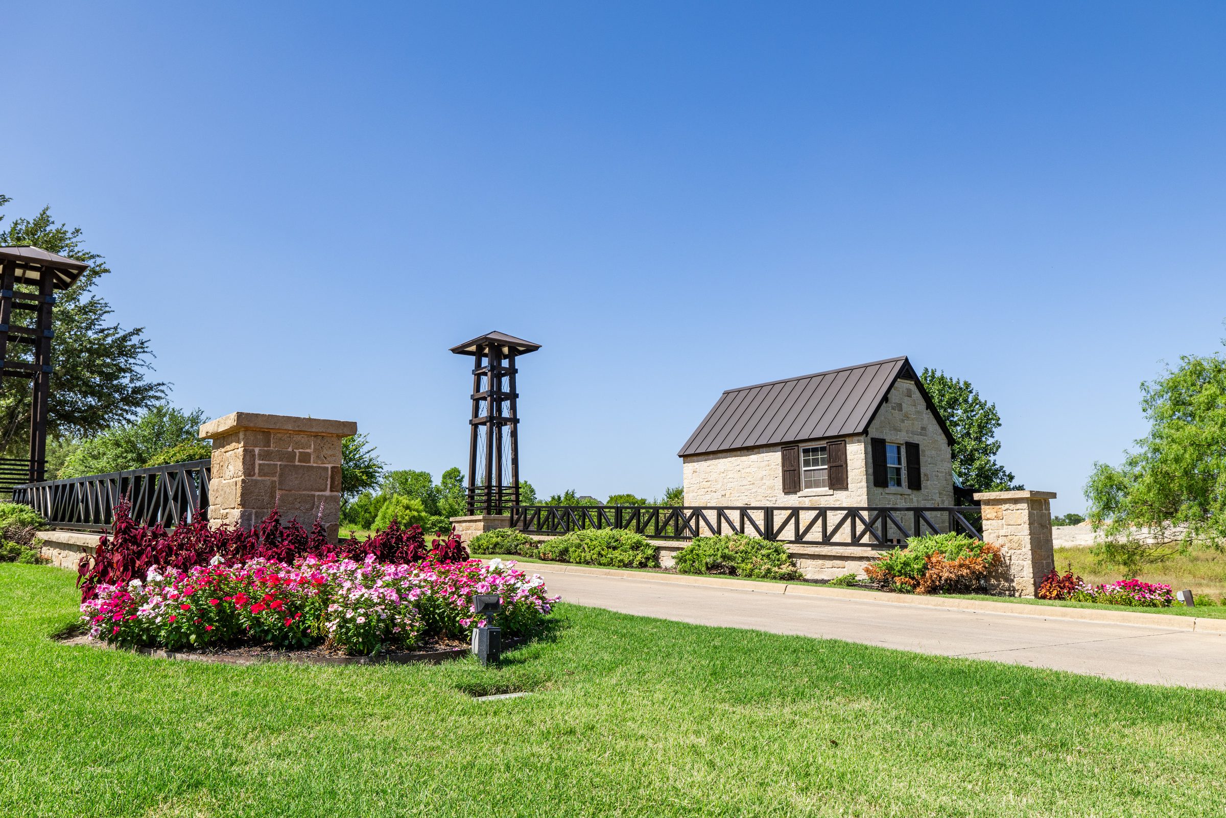 Entrance drive at The Bridges at Preston Crossings with stone pillars, a timber bridge rail, gatehouse and flower beds