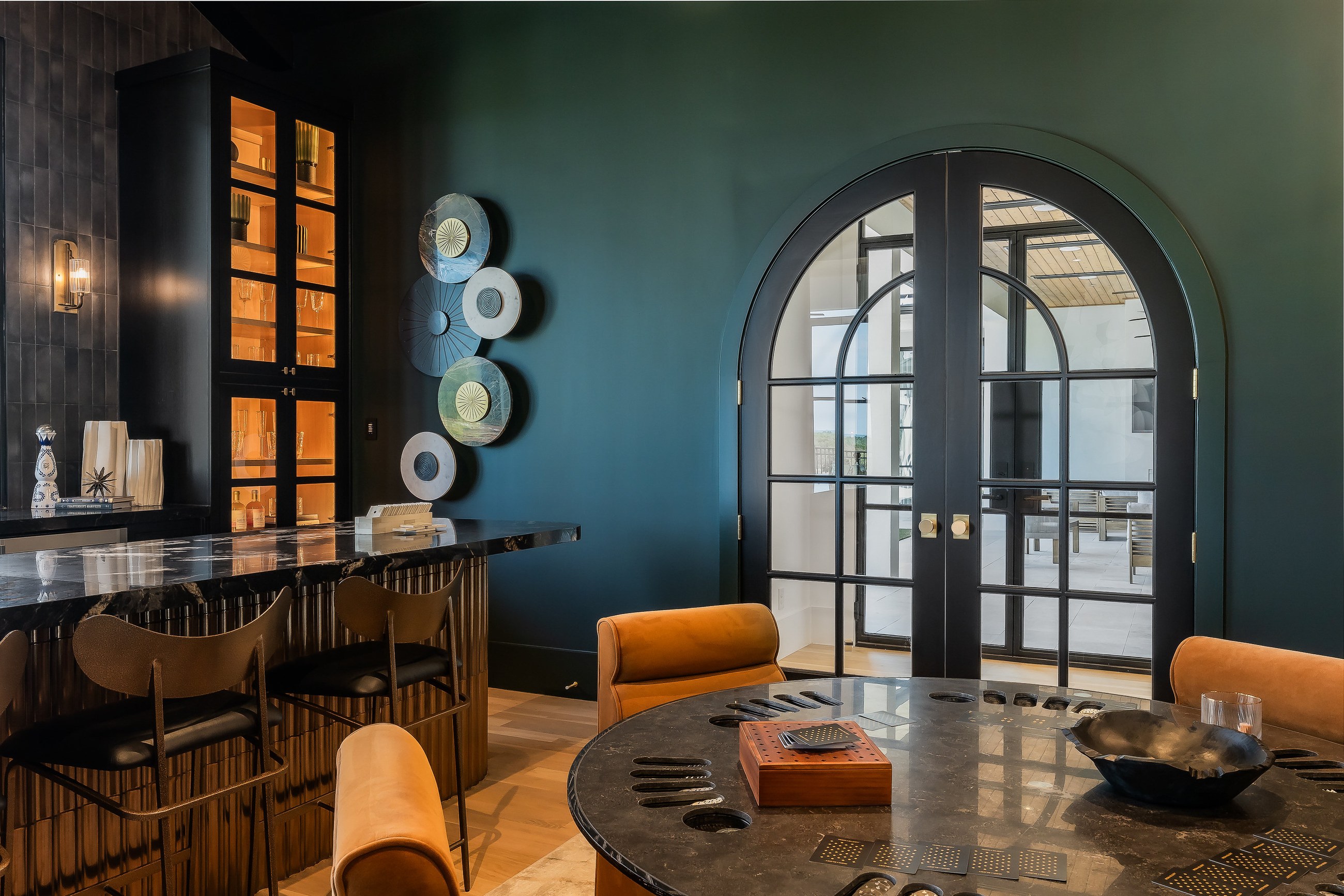 Moody custom bar room with dark cabinetry, brass hardware and arched glass doors