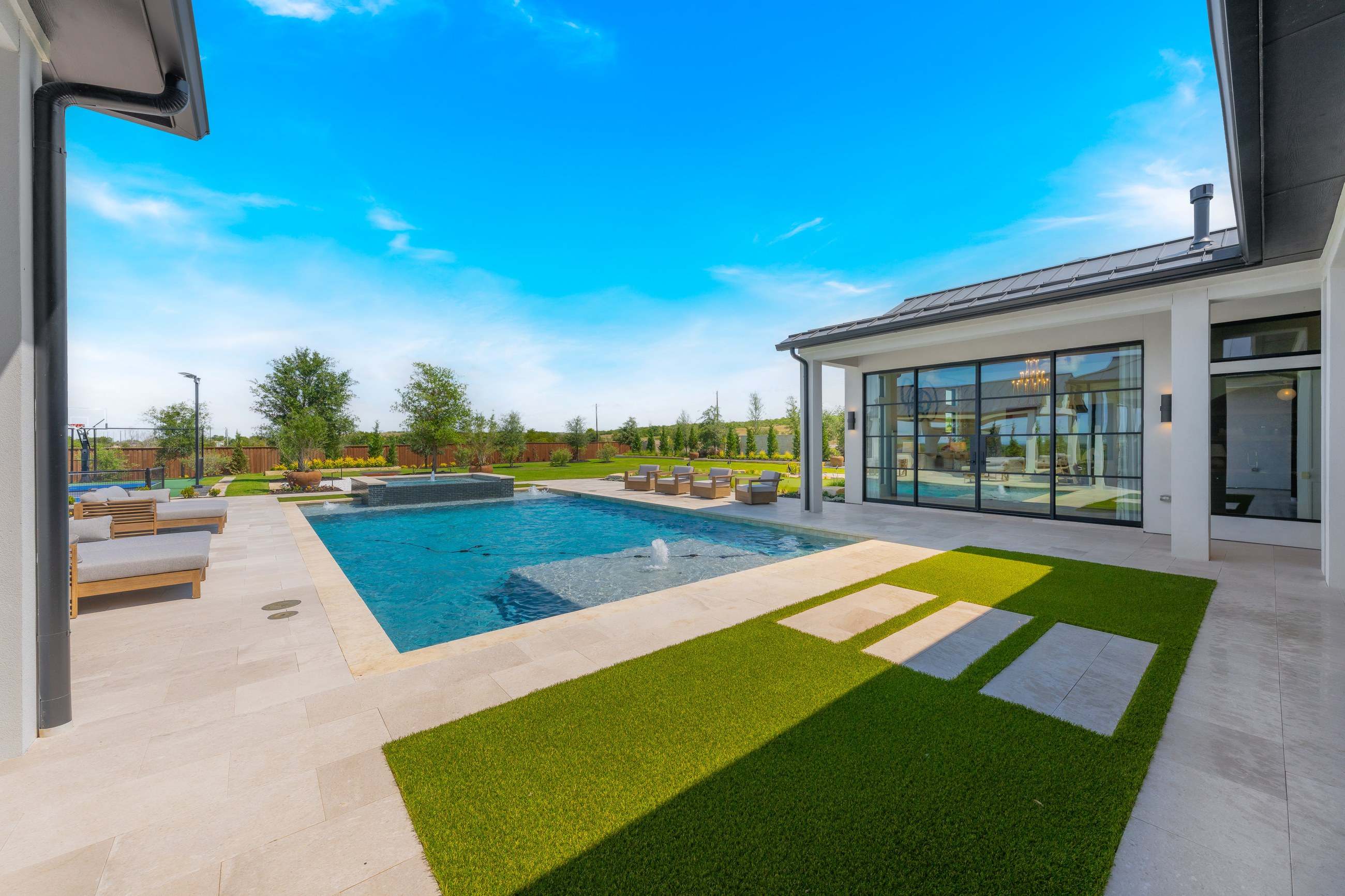 Custom home exterior with expansive glass walls opening onto a covered patio and pool